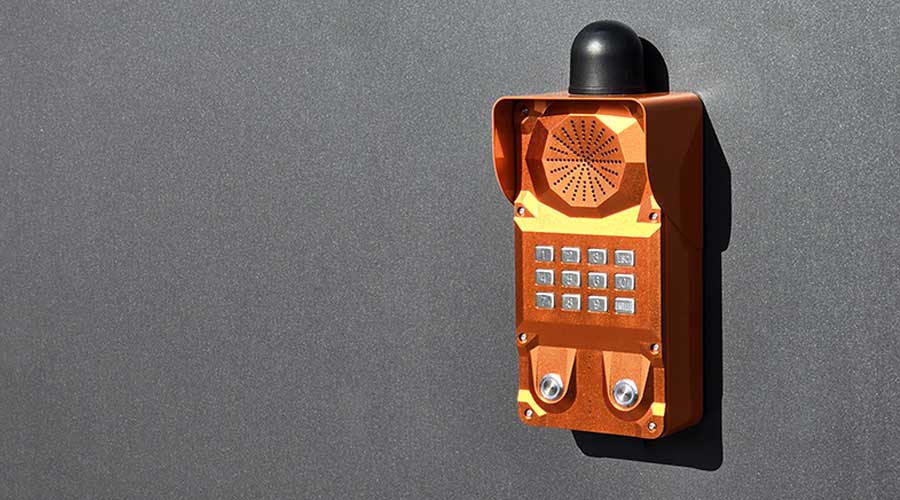 Intercomunicador industrial laranja montado na parede para comunicação em ambientes industriais